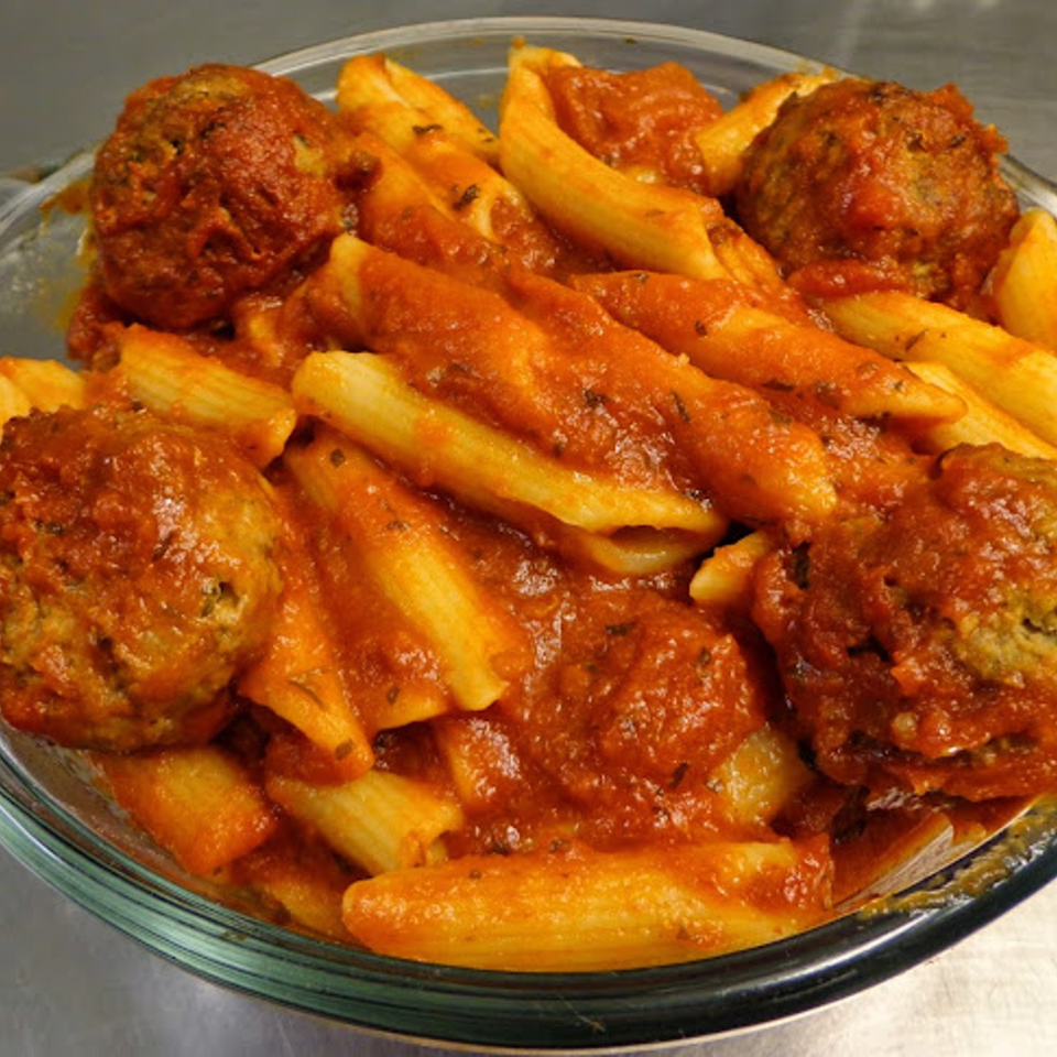 Penne pasta with meatballs and marinara sauce in a clear glass bowl from Pizzano's Pizza & Grinders.