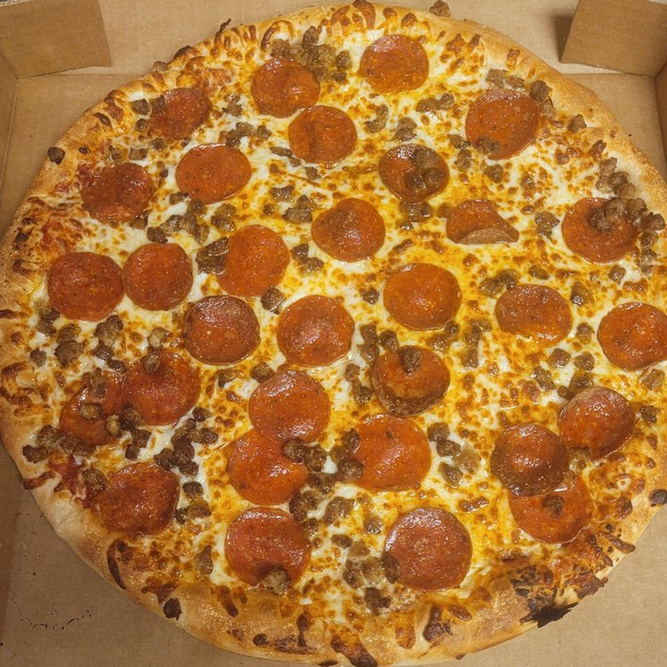 A whole Pizzano's pepperoni and sausage pizza with melted cheese in a cardboard box.