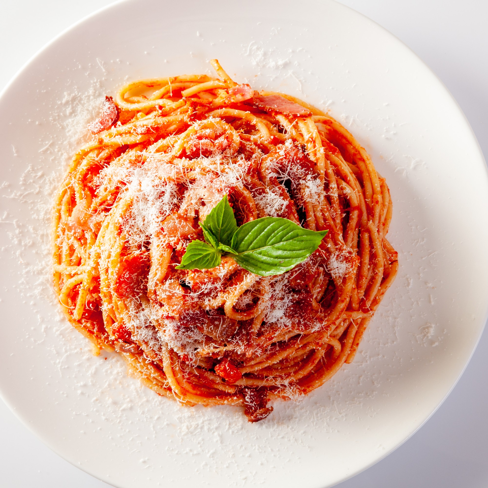 Spaghetti with red sauce, grated cheese, and a fresh basil leaf on a white plate.