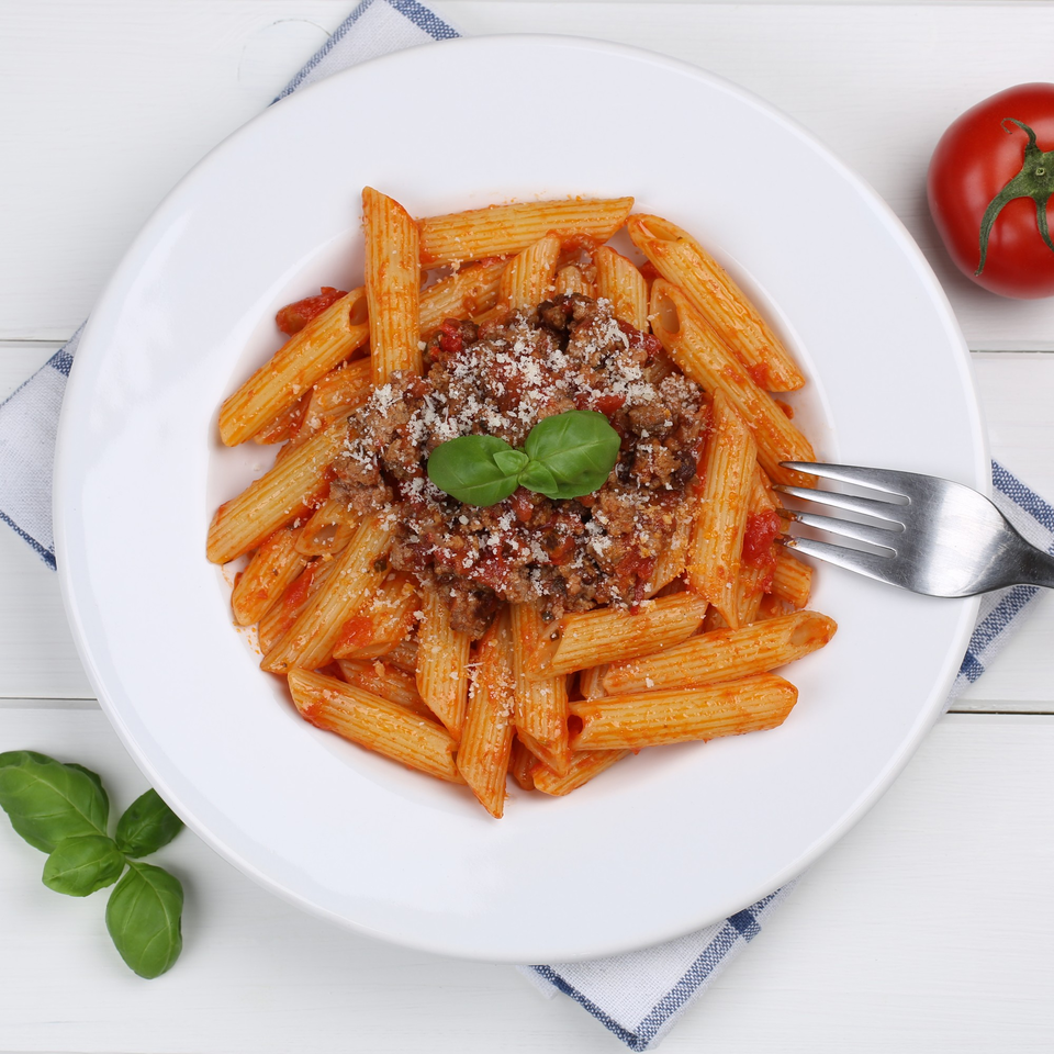 Penne pasta with Bolognese sauce, parmesan cheese, and basil on a white plate.